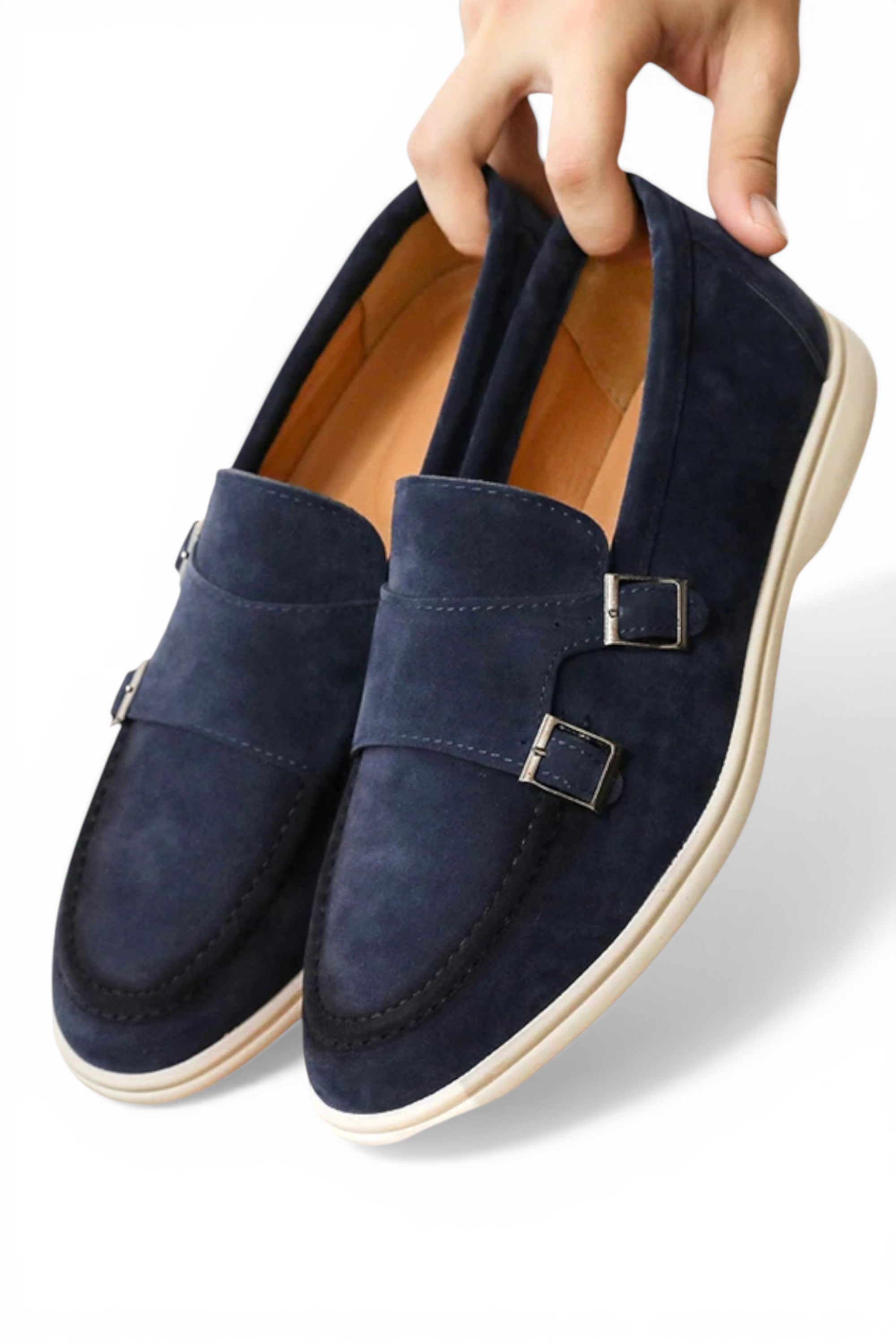 Navy blue loafers with buckles held by a hand on a white background