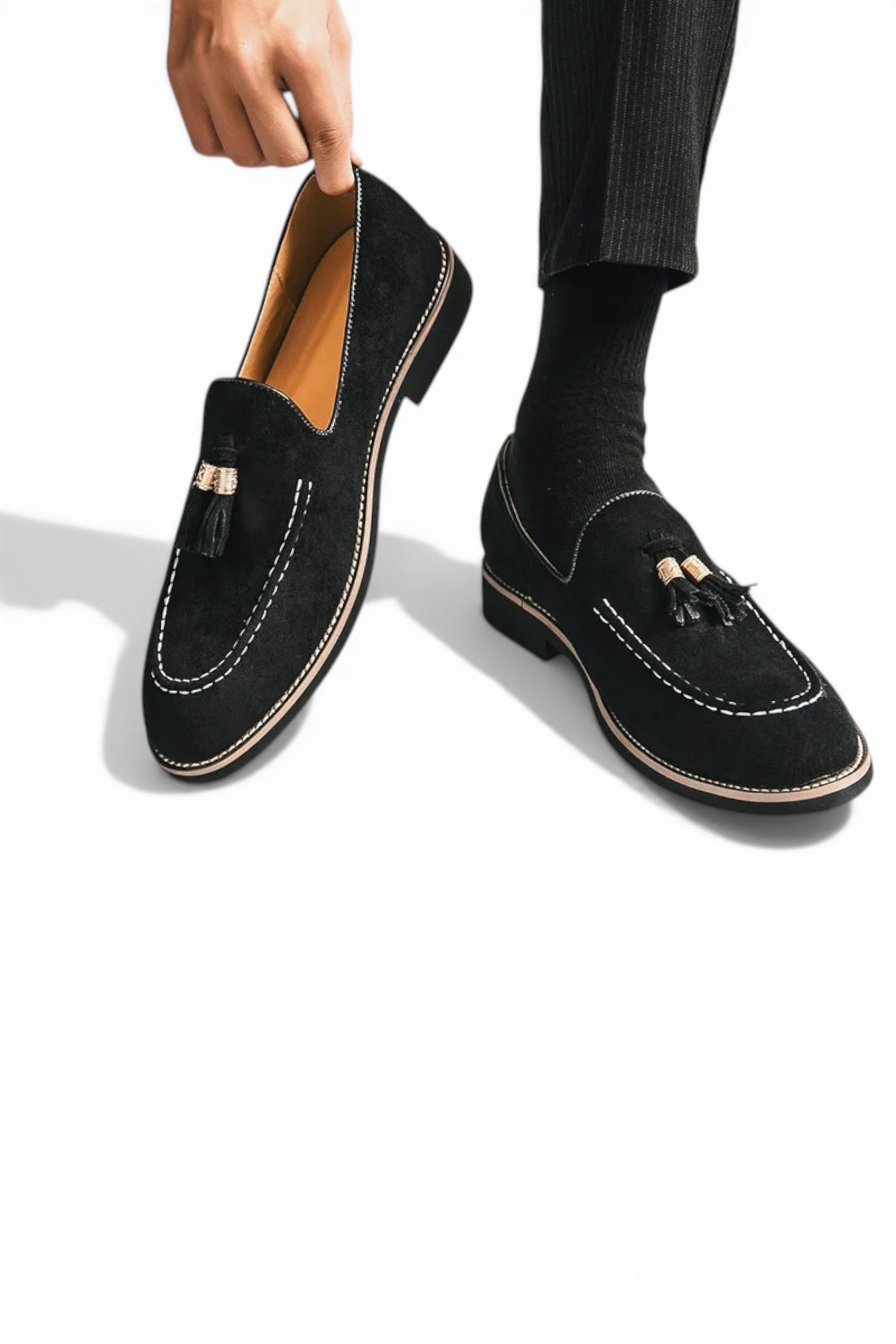 Black loafers with tassels held by a hand on a white background