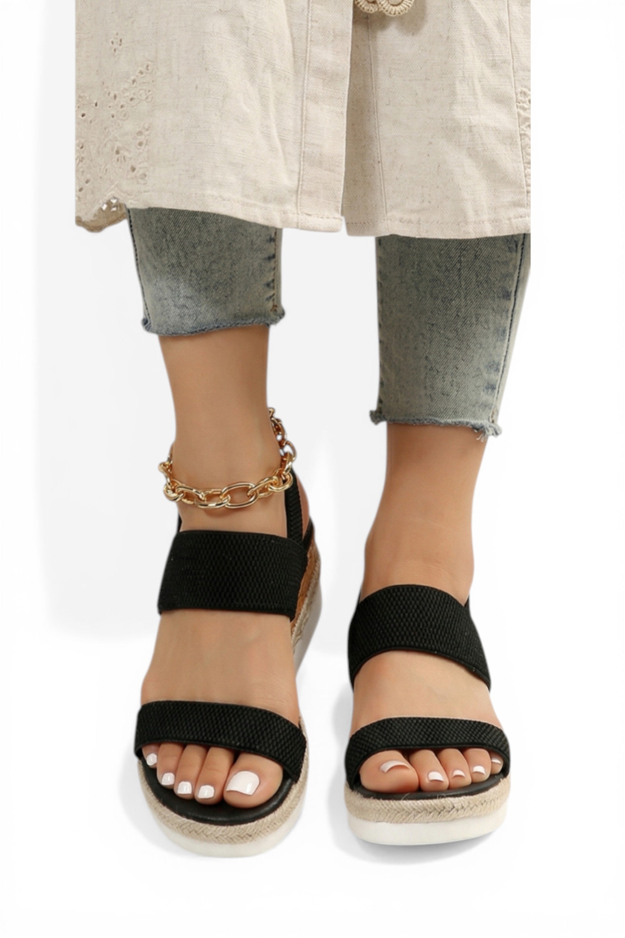 Black wedge sandals worn with rolled-up jeans and a beige coat on a white background