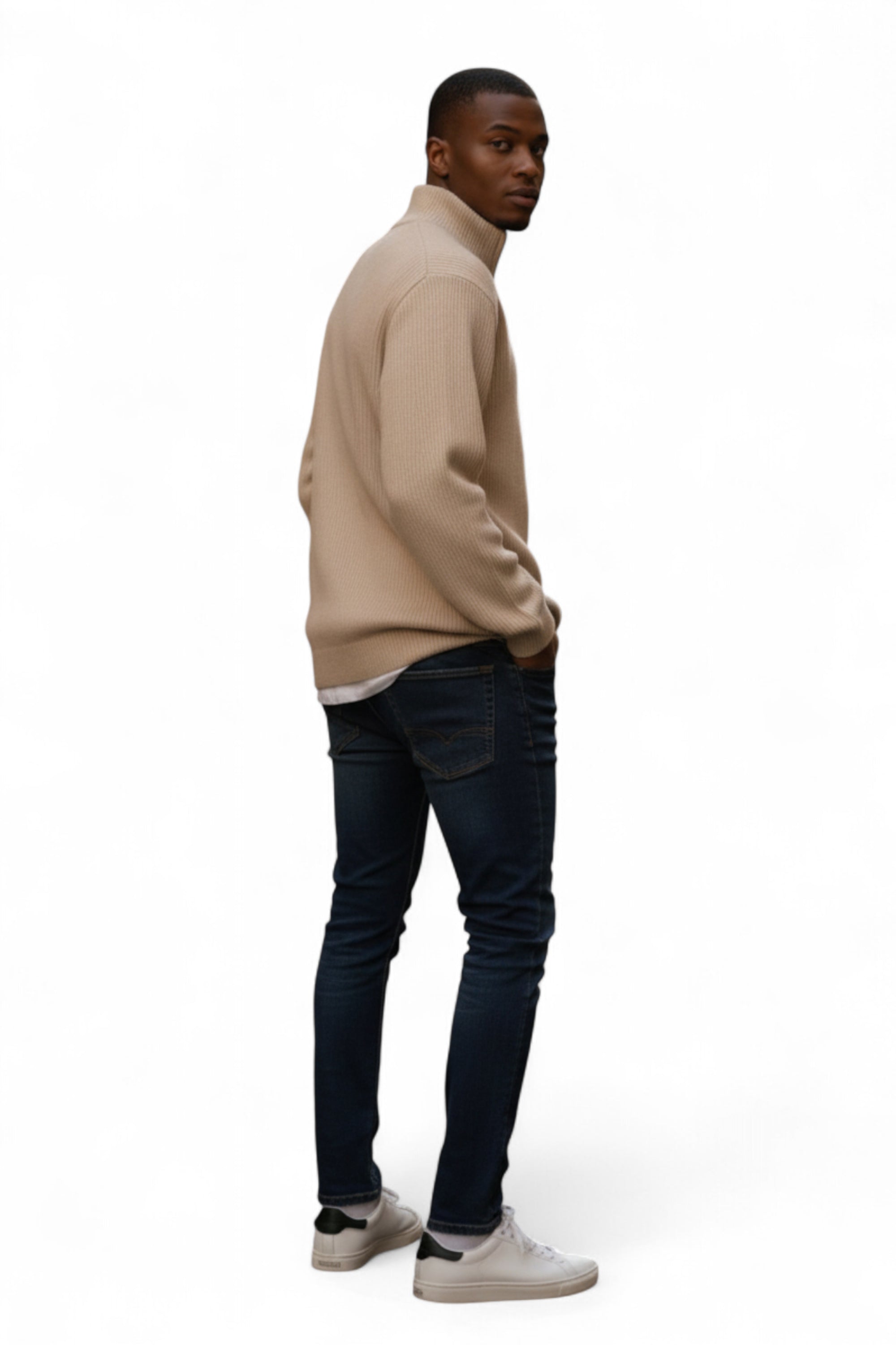 Man wearing a beige sweater and dark jeans on a white background