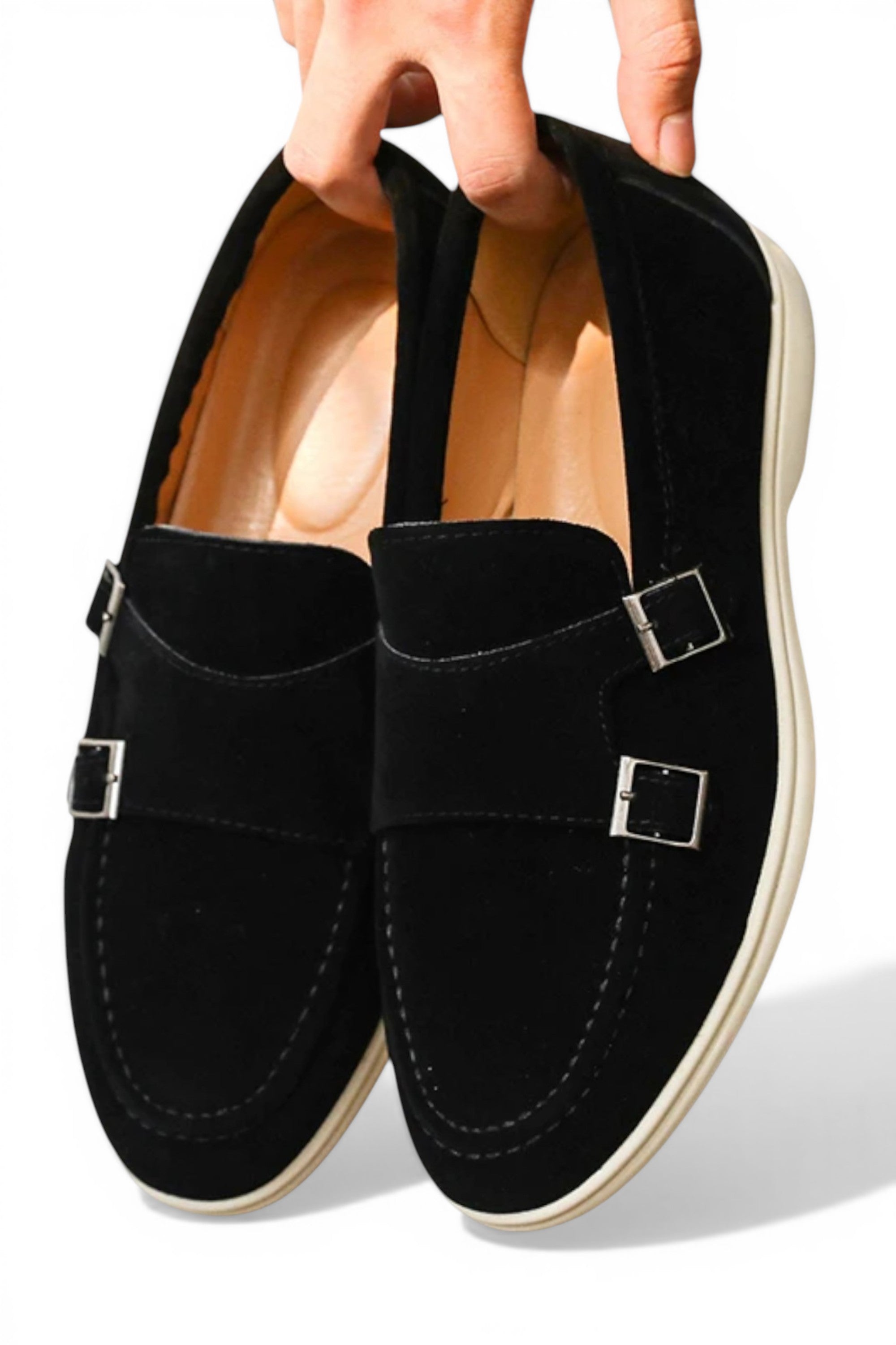 Black loafers with buckles held by a hand on a white background