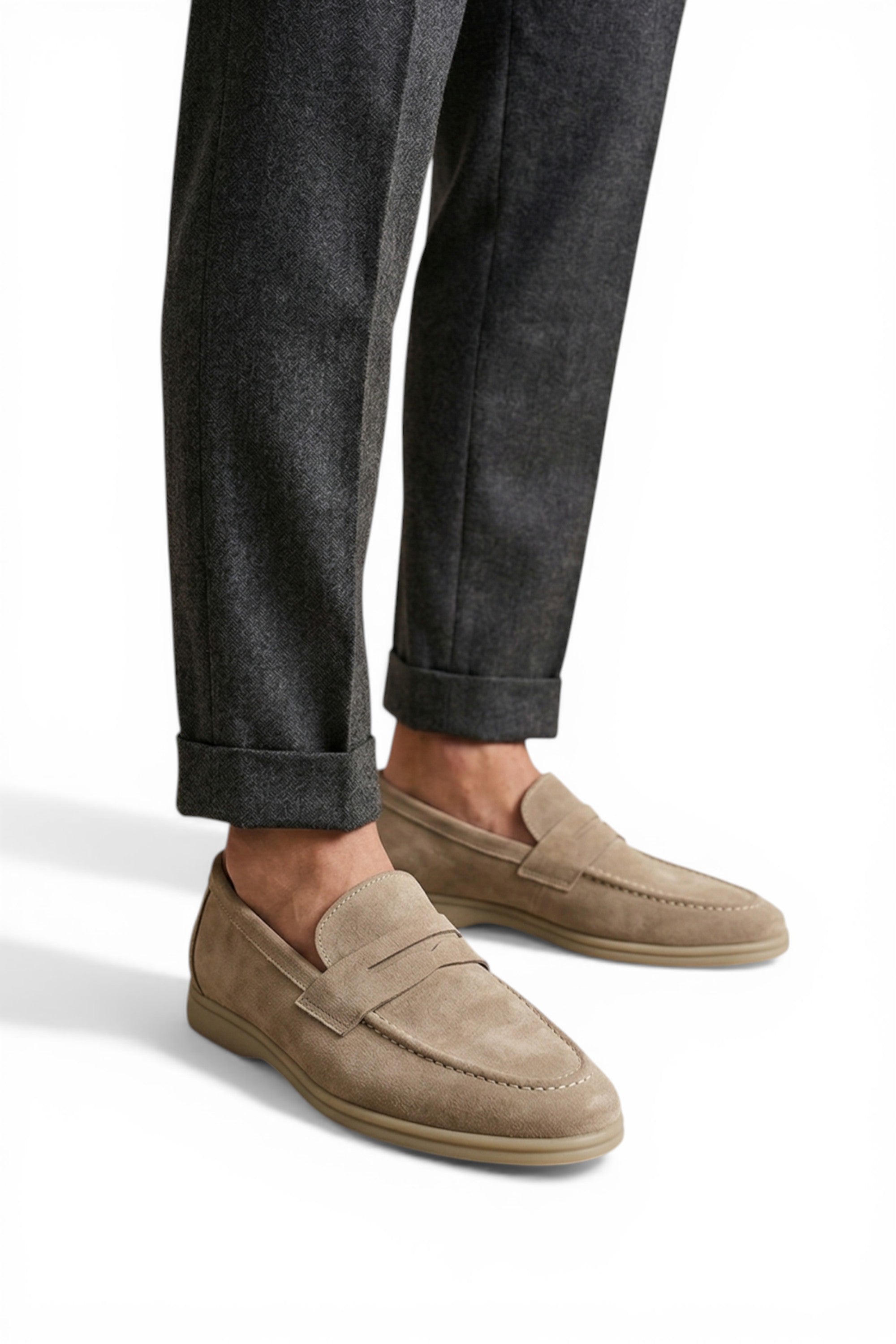 Beige loafers worn with dark gray pants on a white background